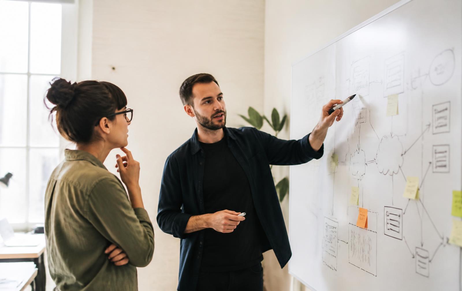 Two colleagues reviewing a hand-drawn software architecture diagram on a whiteboard